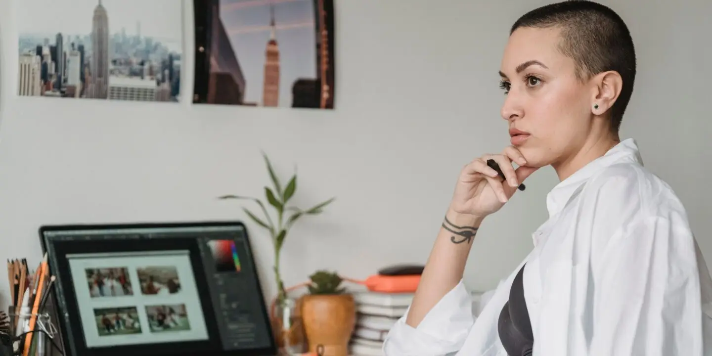Graphic designer reflecting at her workspace while reviewing creative work on a laptop after a professional setback.