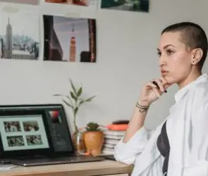 Graphic designer reflecting at her workspace while reviewing creative work on a laptop after a professional setback.