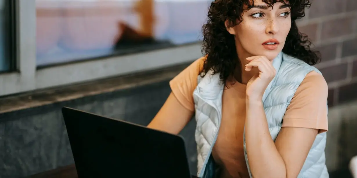 Designer thinking at a laptop while evaluating the potential of a new creative business idea before launch.