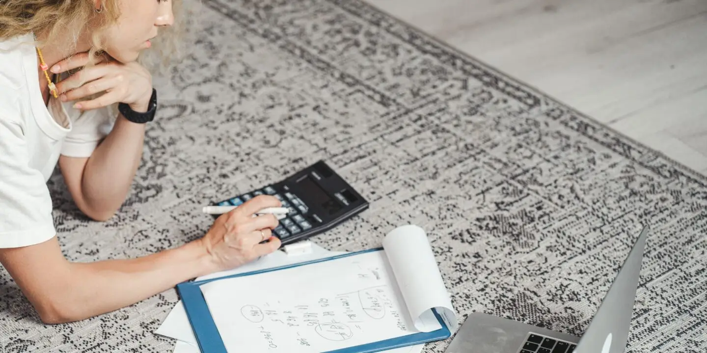 Freelance designer calculating project finances and monthly expenses while working from home.