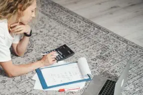 Freelance designer calculating project finances and monthly expenses while working from home.