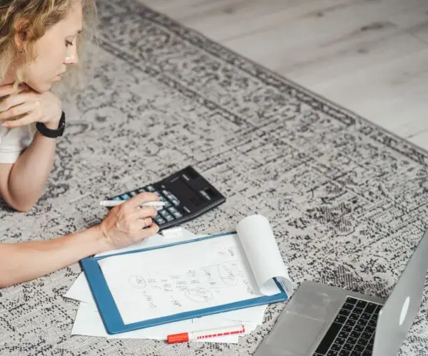 Freelance designer calculating project finances and monthly expenses while working from home.